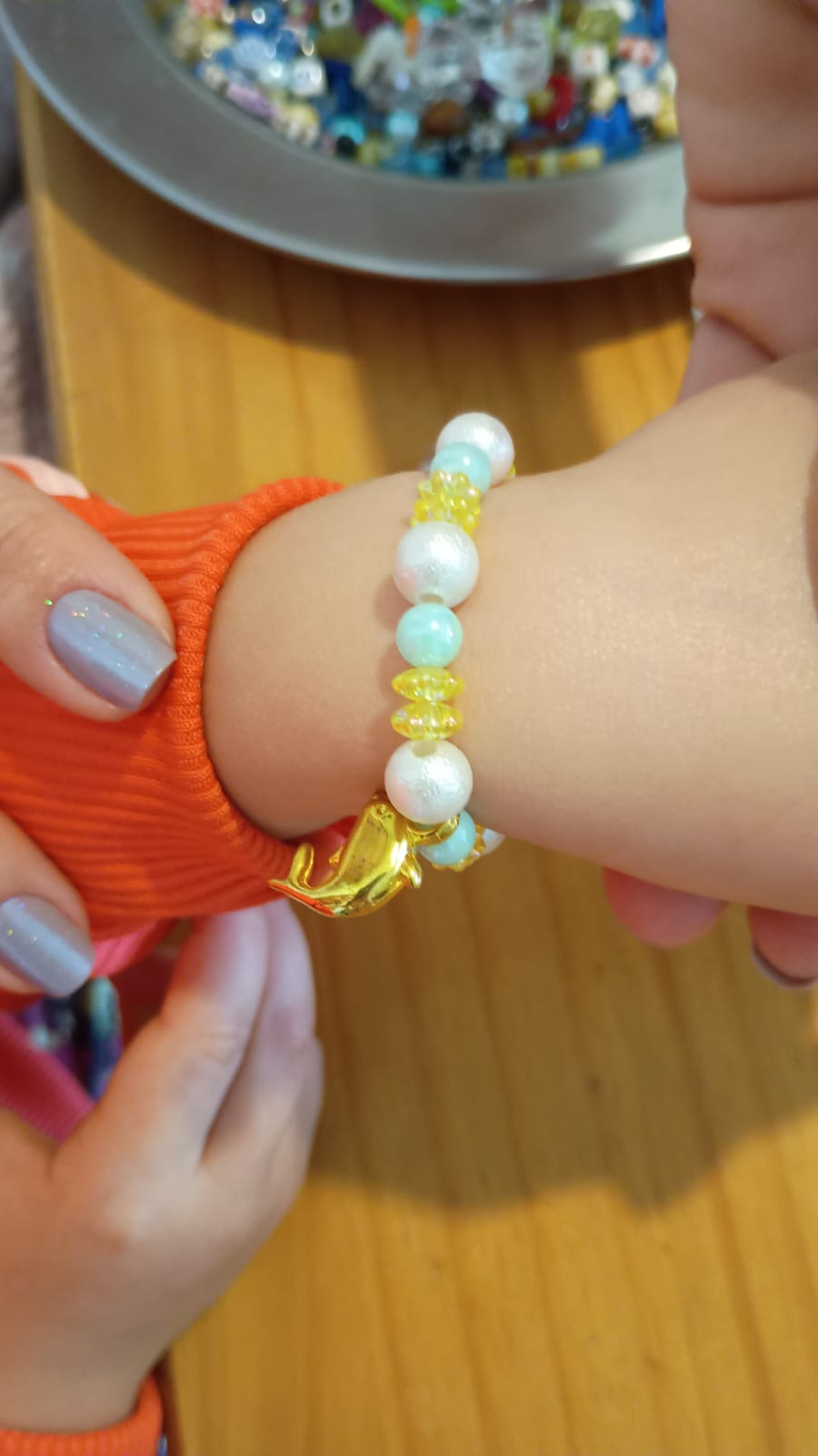 Pulseira no pulso com miçangas coloridas e pingente de golfinho